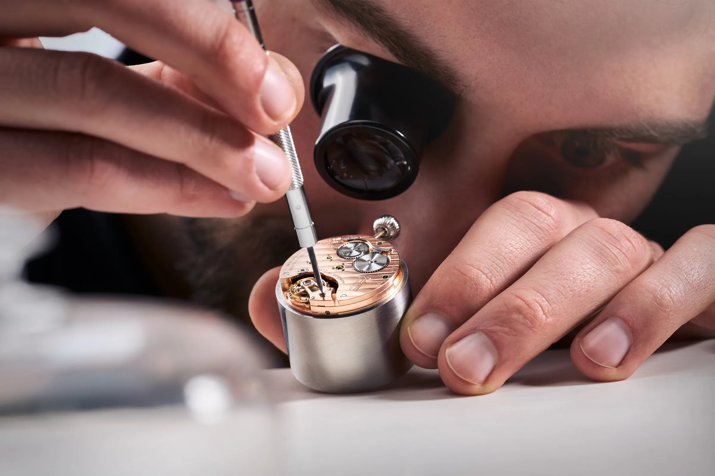 Watchmaker with loupe examining a rose gold movement at the Tutima Manufaktur