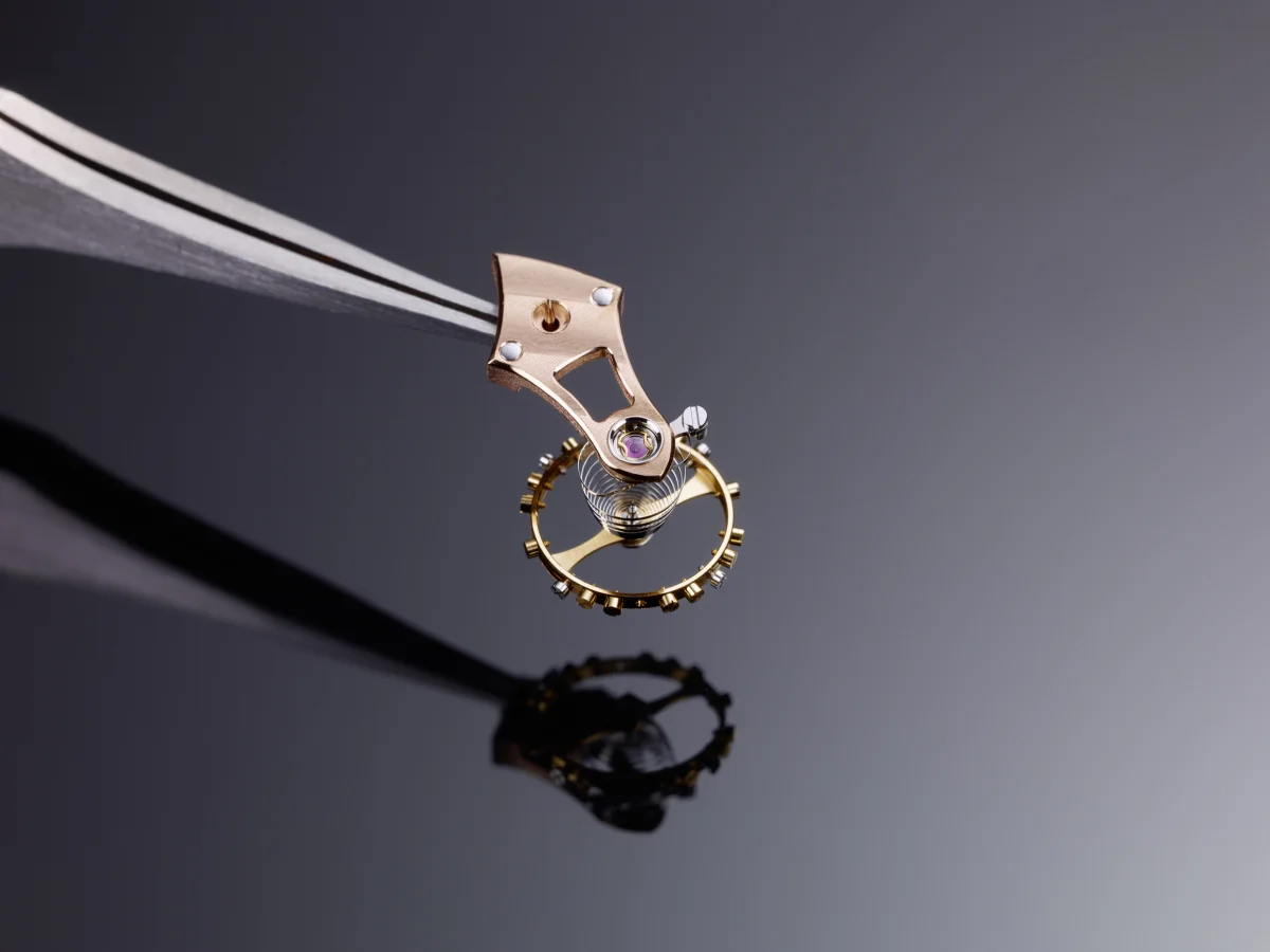 Caliber 617 balance and cock held with tweezers — Breguet overcoil visible