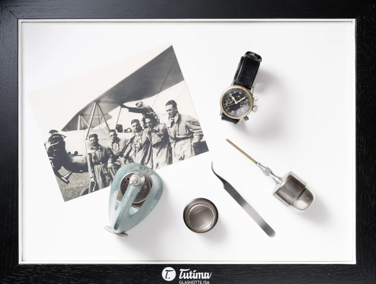Framed flat-lay with Tutima Glashütte/SA branding and vintage aviation photograph — founding meets aviation DNA