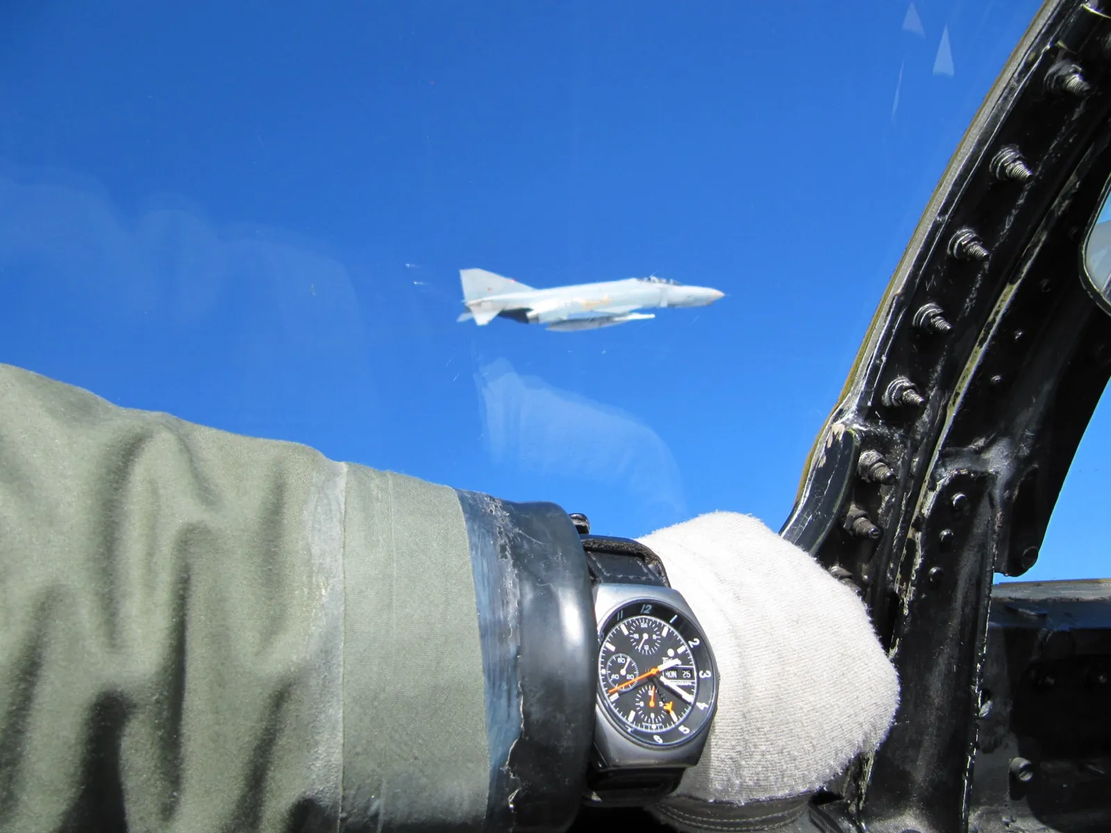 NATOクロノグラフを着けたパイロットの手首、青空を背景にウィングマンのF-4ファントム