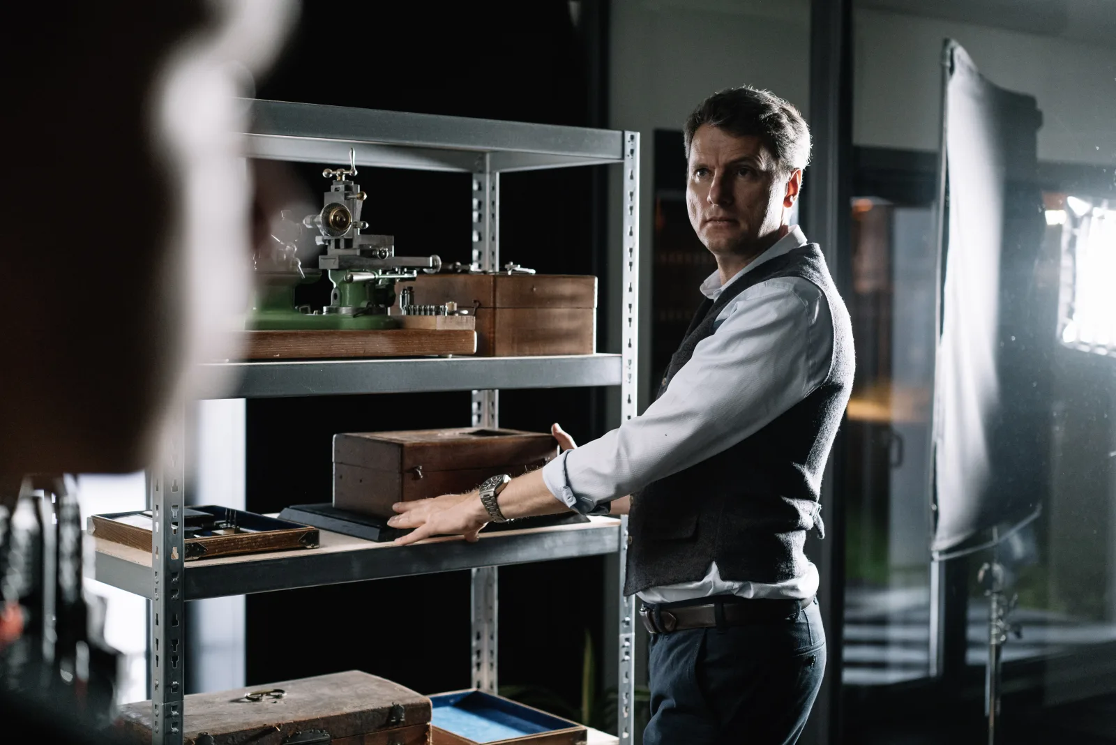 Cinematic portrait — man with vintage watchmaking tools and wooden cases in the Glashütte workshop