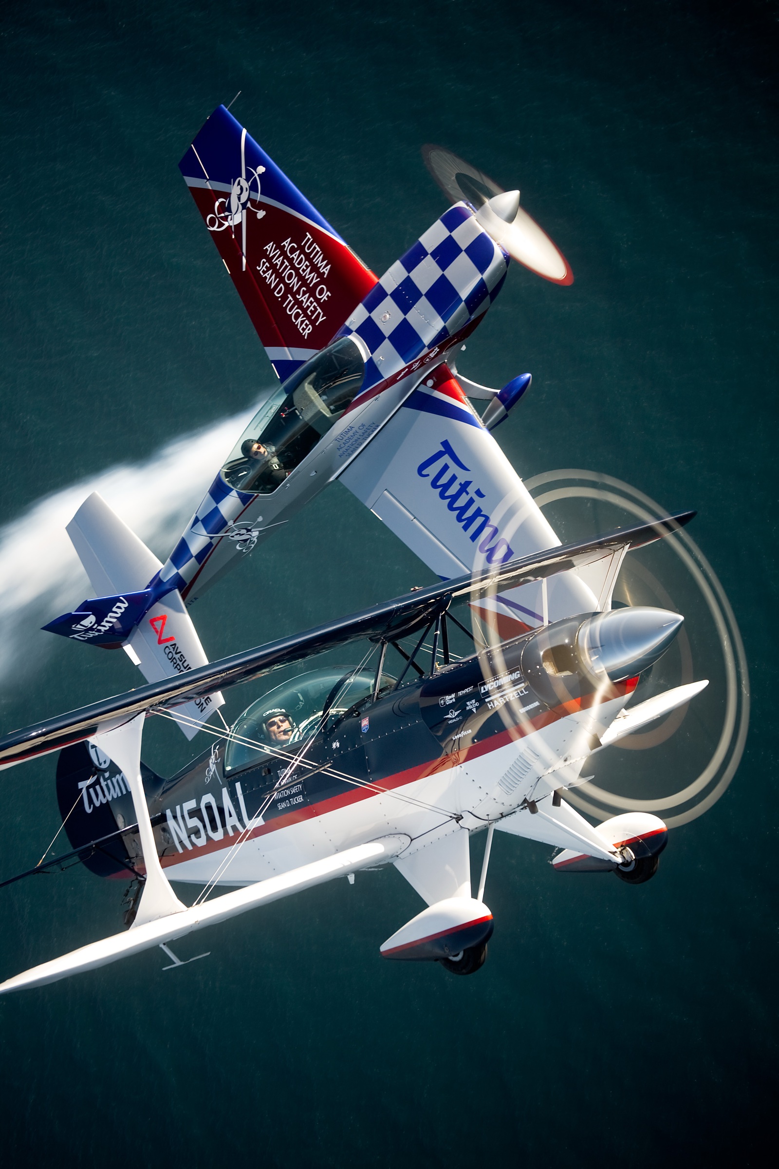 Three Tutima-branded biplanes in formation over turquoise ocean