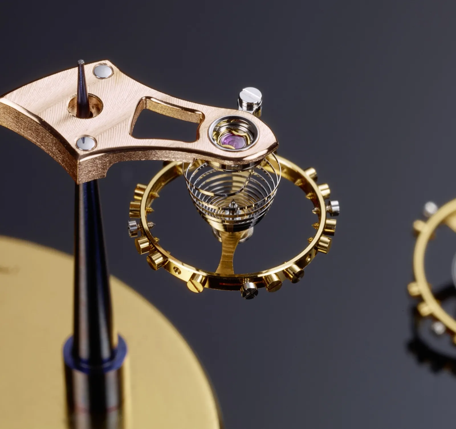 Cal. 617 balance wheel and cock — gold balance, hairspring, and ruby jewel held in tweezers